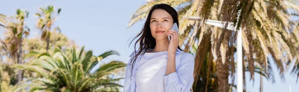 Brunette woman in blue shirt talking on mobile phone in park, banner — Stock Photo