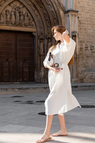 Pleine longueur de jeune rousse femme en robe tenant sac à main sur la rue de valencia — Photo de stock