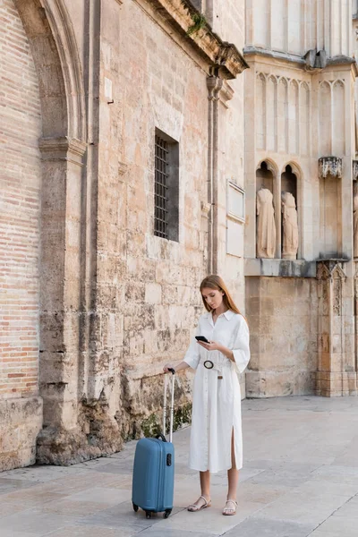 Vollständige Länge der rothaarige Frau, die mit Gepäck steht und Smartphone während der Suche geolocation in valencia — Stockfoto