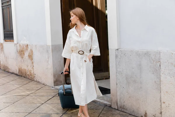 Young redhead woman in white dress walking with hand in pocket on street in valencia — Stock Photo