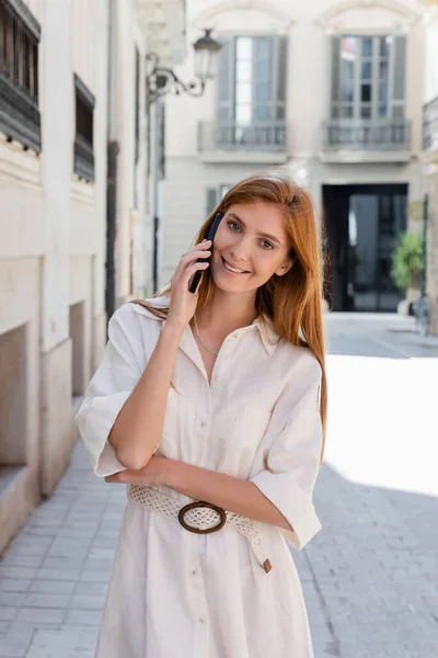 Lächelnde rothaarige Frau im Kleid, die auf dem Handy in Valencia spricht — Stockfoto