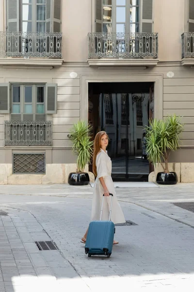 Full length of young woman in dress walking with baggage on european street in Valencia — Stock Photo