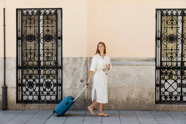 Volle Länge der jungen Frau im Sommerkleid zu Fuß mit Gepäck und Pappbecher in der Nähe von Gebäude in Valencia — Stockfoto