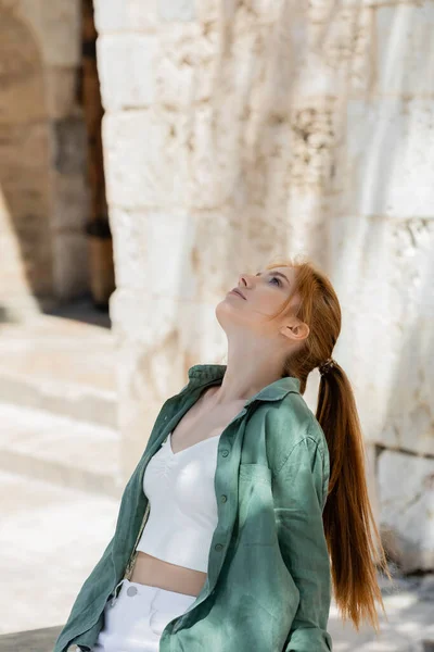 Giovane donna con i capelli rossi in camicia di lino verde seduta su una panchina di cemento — Foto stock