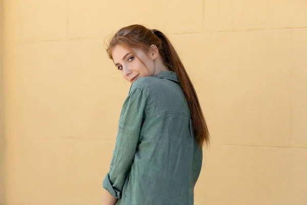 Молодая женщина в зеленой льняной рубашке позирует возле бежевой стены на улице — стоковое фото