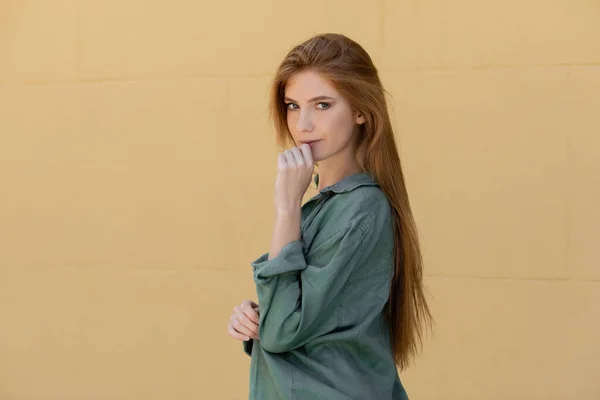 Jeune rousse femme en lin vert chemise posant près du mur beige — Photo de stock