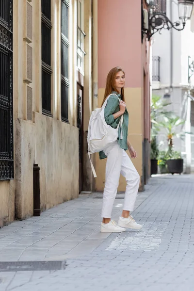 Viajero contento y pelirrojo con mochila caminando por la calle de valencia - foto de stock