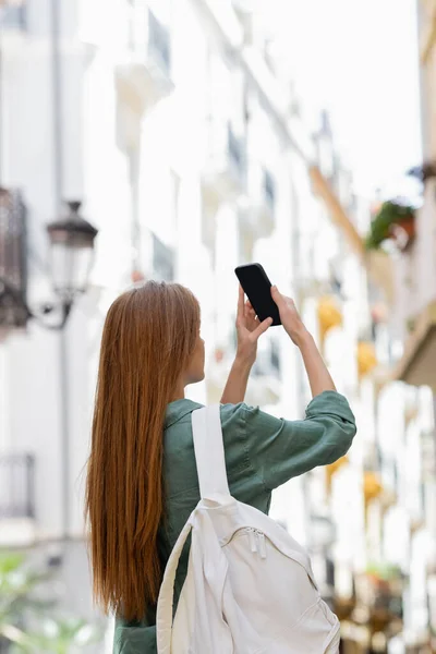 Jovem viajante ruiva com mochila tirando foto no smartphone na rua urbana de valência — Fotografia de Stock
