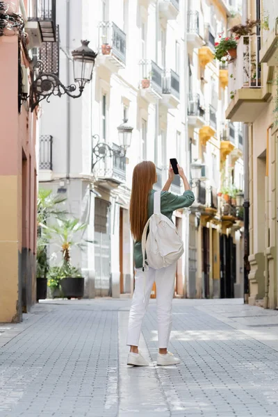 Rotschopf Reisender mit Rucksack fotografiert auf Smartphone auf der städtischen Straße von Valencia — Stockfoto