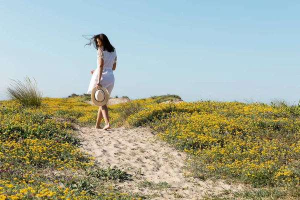 Жінка тримає сонцезахисний капелюх стоячи на пляжі. — стокове фото