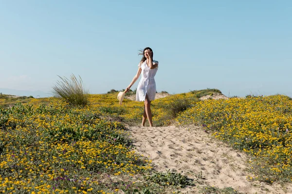 Junge Frau im Kleid mit Sonnenhut beim Spaziergang am Strand — Stockfoto