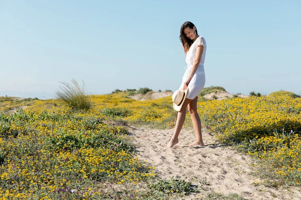 Happy young woman looking at straw hat on sandy beach — Stock Photo