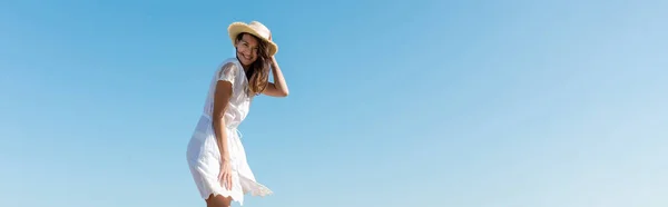 Giovane donna in abito bianco e cappello da sole sorridente alla fotocamera con cielo sullo sfondo, striscione — Foto stock