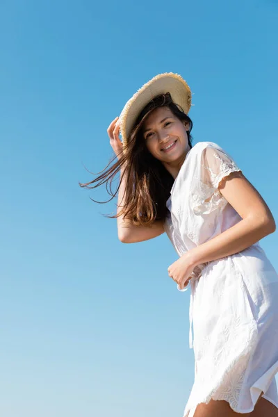 Vista de ángulo bajo de la mujer positiva en vestido sosteniendo sombrero de paja con el cielo en el fondo - foto de stock