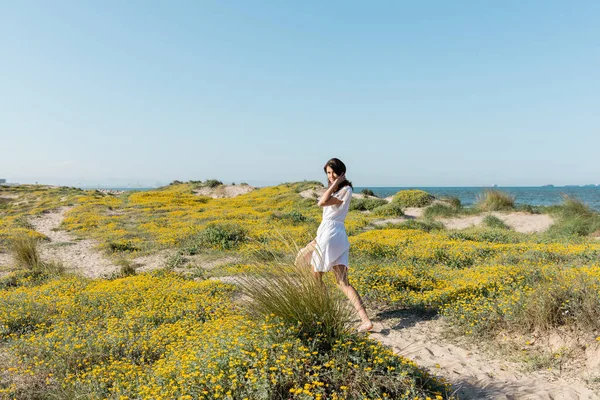 Молода жінка в одязі дивиться на камеру біля квітів на пляжі — стокове фото