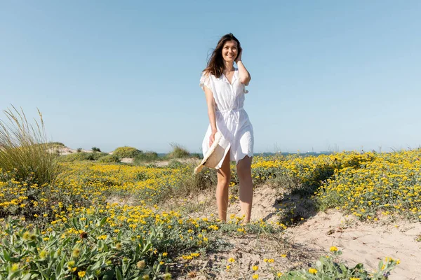 Positive Frau im weißen Sommerkleid mit Strohhut am Strand — Stockfoto