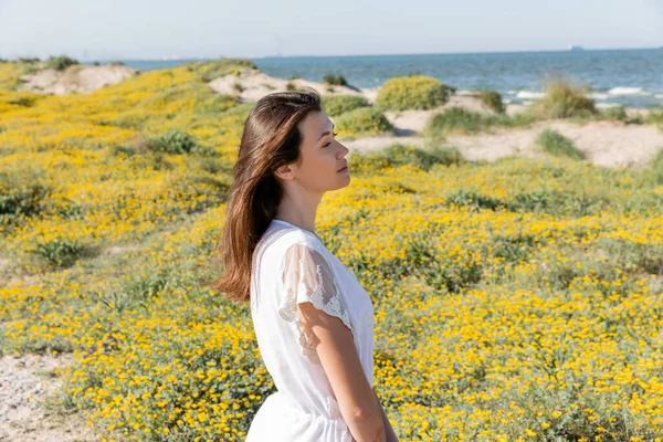 Vista lateral da jovem mulher de vestido branco em pé na praia turva — Fotografia de Stock