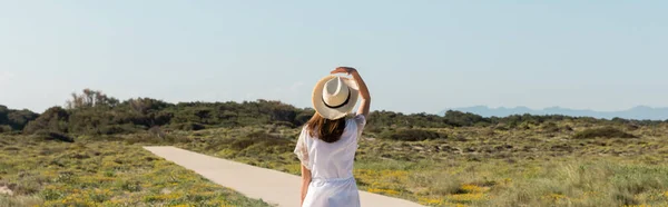 Вид сзади женщины в соломенной шляпе идущей по тропинке по пляжу, баннер — стоковое фото