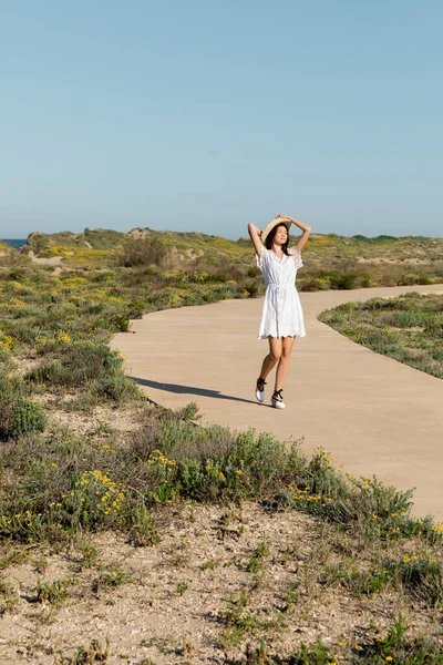 Junge Frau in Sommerkleid und Sonnenhut läuft am Strand auf Gehweg — Stockfoto