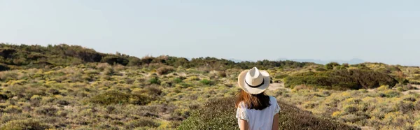 Back view of young woman in straw hat standing on beach with grass, banner — Stock Photo