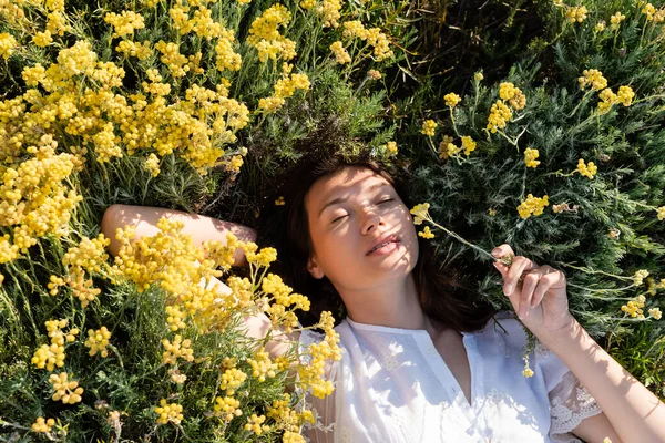 Vue du dessus de la jeune femme allongée sur la pelouse avec des fleurs jaunes — Photo de stock