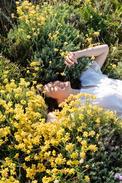 Vista de ángulo alto de la mujer alegre acostada en el césped con flores amarillas - foto de stock