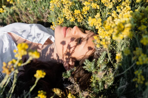 Mujer joven cerrando los ojos mientras está acostada en el prado con flores - foto de stock