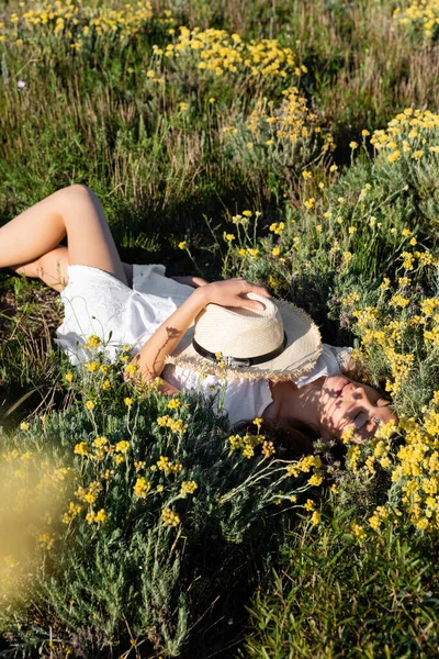 Высокоугольный вид женщины в летнем платье, держащей солнечную шляпу, лежа на диване — стоковое фото