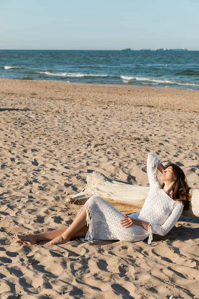 Mulher de malha vestido deitado perto de madeira log na praia — Fotografia de Stock