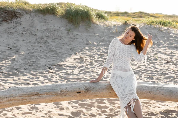 Brünette Frau im Strickkleid sitzt auf Holzklotz am Strand — Stockfoto