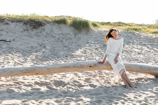 Junge Frau in gestricktem Sommerkleid ruht auf Holzklotz am Strand — Stockfoto