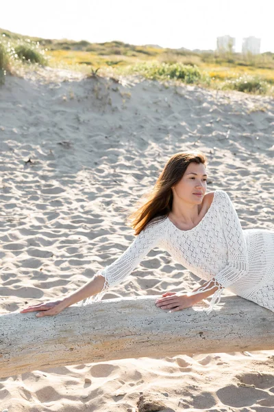 Frau in sommerlichem weißen Kleid posiert auf Holzklotz am Strand — Stockfoto