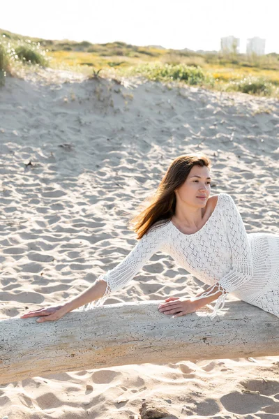 Mujer en vestido blanco de verano posando sobre tronco de madera en la playa - foto de stock