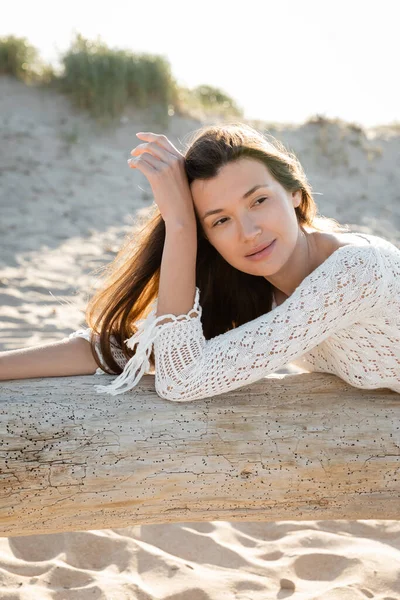 Porträt einer brünetten Frau, die auf einem Holzklotz am Sandstrand liegt — Stockfoto