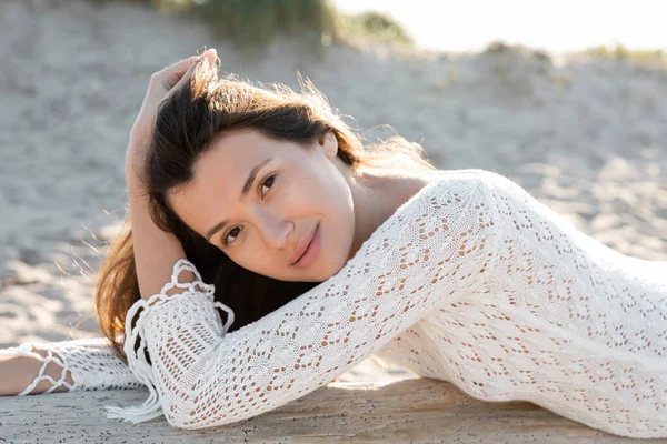 Porträt einer hübschen Frau im Strickkleid, die in die Kamera blickt, während sie am Strand auf einem Holzklotz liegt — Stockfoto