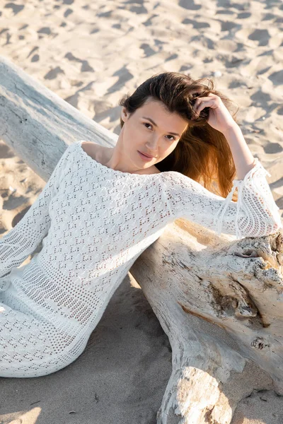 High angle view of young woman in summer knitted dress looking at camera near log on beach — Stock Photo