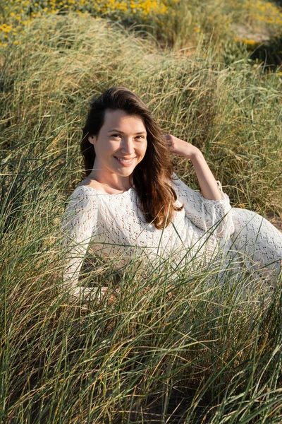 Smiling woman in knitted dress looking at camera while lying on grass on beach — Stock Photo