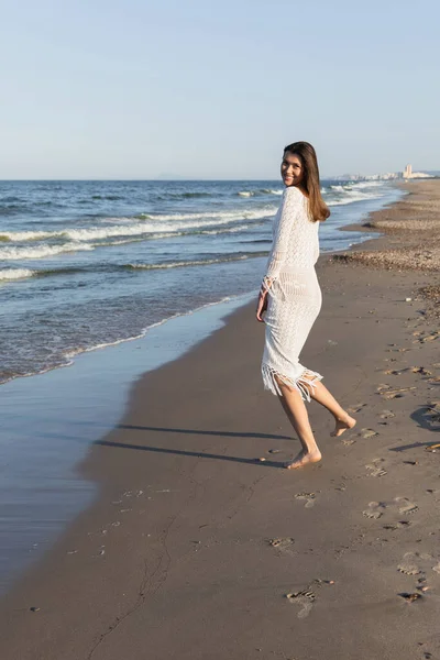 Lächelnde Frau im Strickkleid blickt am Strand am Meer in die Kamera — Stockfoto