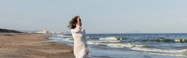 Вид сбоку на веселую молодую женщину в трикотажном платье, смотрящую на море, баннер — стоковое фото