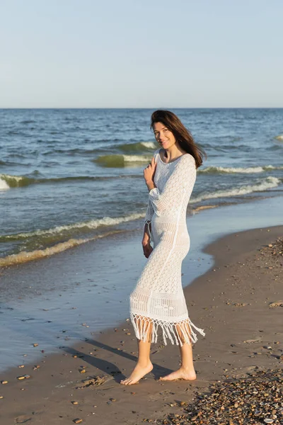 Femme pieds nus en robe tricotée debout sur la plage près de la mer — Photo de stock