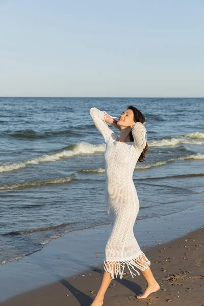 Pretty young woman in knitted dress walking on sand near sea — Stock Photo