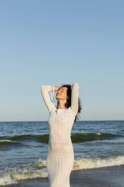 Femme souriante en robe blanche tricotée debout près de la mer — Photo de stock