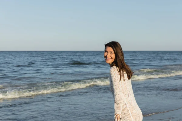 Heureuse femme brune regardant la caméra près de la mer floue — Photo de stock