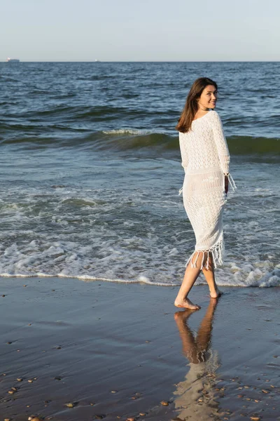 Hübsche Frau schaut in Kamera, während sie am Strand am Meer spaziert — Stockfoto