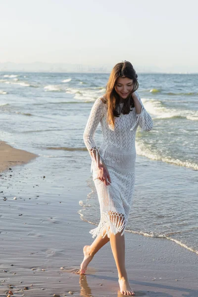 Positive young woman in summer dress walking on wet sand on beach — Stock Photo