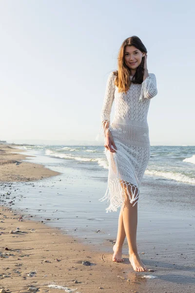 Hübsche junge Frau blickt am Strand mit Meer im Hintergrund in die Kamera — Stockfoto