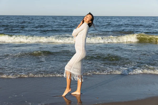 Hübsche Frau schließt die Augen, während sie am Strand im Meerwasser steht — Stockfoto