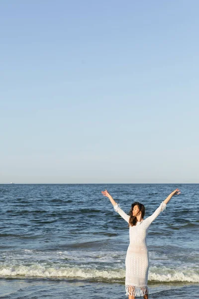 Femme positive en robe debout près de la mer avec un ciel bleu à l'arrière-plan — Photo de stock