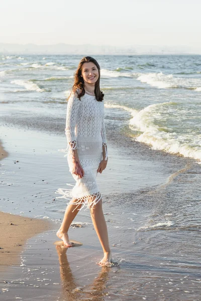 Lächelnde Frau im Strickkleid blickt am Sandstrand in die Kamera — Stockfoto