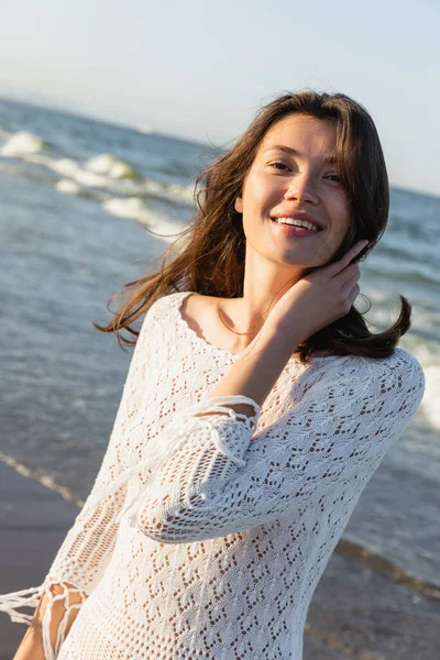 Porträt einer brünetten Frau im Sommerkleid, die in die Kamera am verschwommenen Meer blickt — Stockfoto